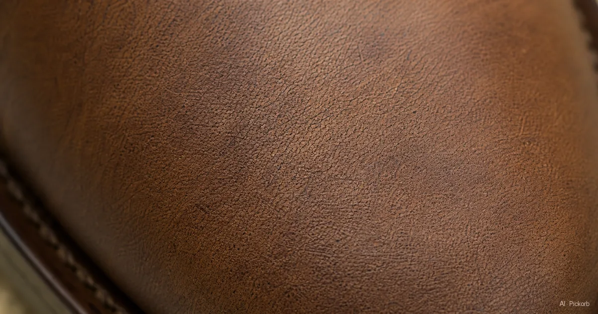A close-up of leather shoe upper showing the natural grain texture — visible pores, slight irregular markings, soft matte surface (AI generated illustration)